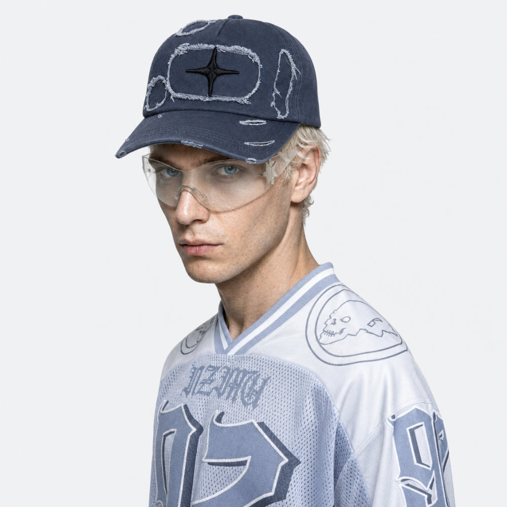 A model wearing a navy blue distressed baseball cap with a black star logo, paired with a white and blue sports jersey, against a light gray background.