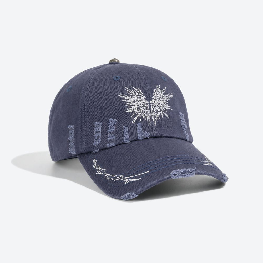A navy blue distressed baseball cap with a white embroidered moth, shown from a three-quarter angle revealing the ripped detailing on the crown