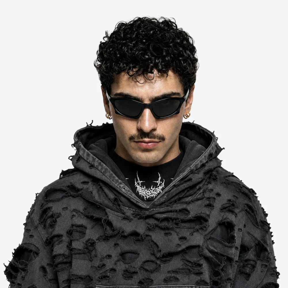 VYSER black distressed oversized hoodie with ripped texture, styled with sleek cat-eye sunglasses and gold hoops.