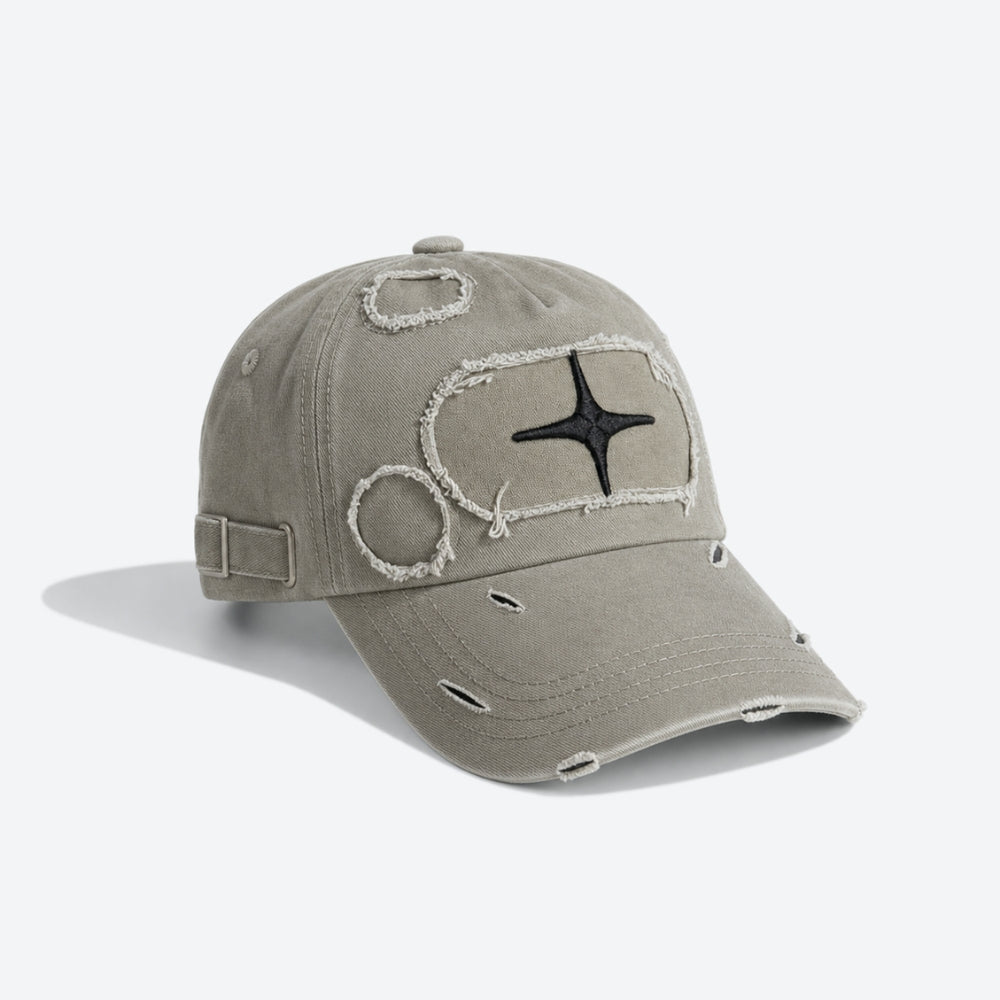 A distressed baseball cap in a muted grayish beige color, featuring a black embroidered star on a frayed outline patch on the front, with additional distressed details including ripped fabric edges and a side strap closure.