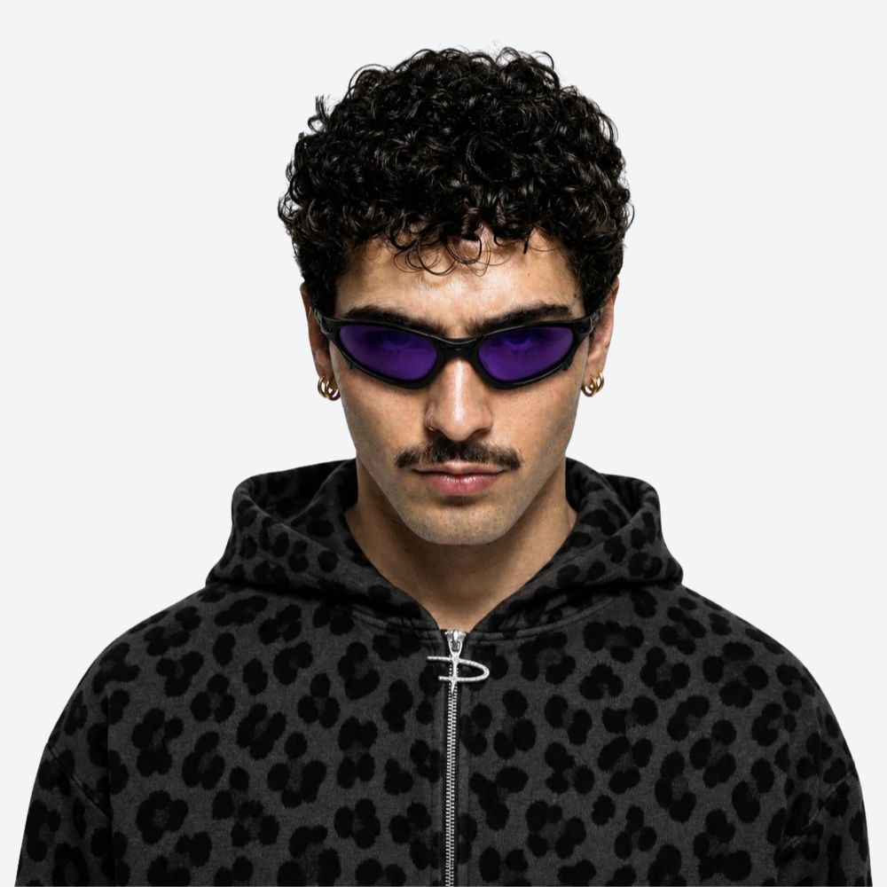 Person wearing a black leopard print hoodie and VYSER Sunglasses with a black frame and purple lenses on a white background