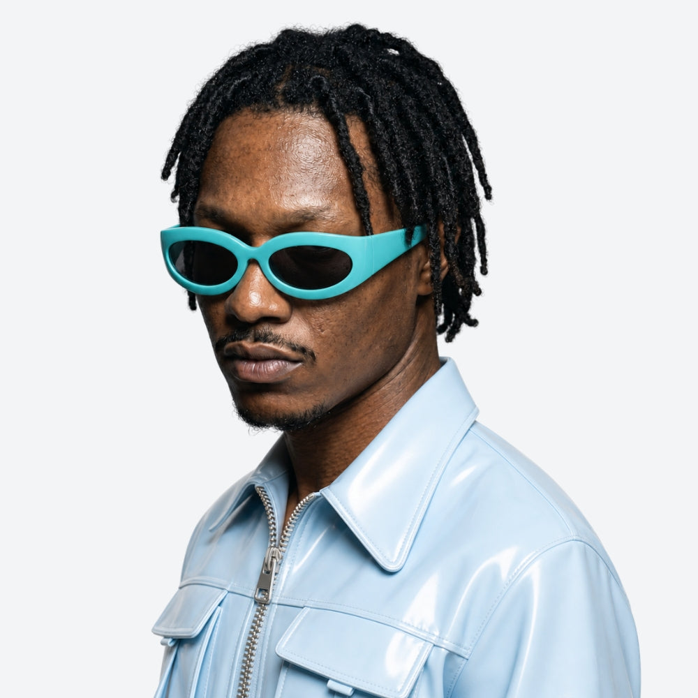 Person wearing VYSER Turquoise sunglasses with black lenses and a light blue jacket on a white background