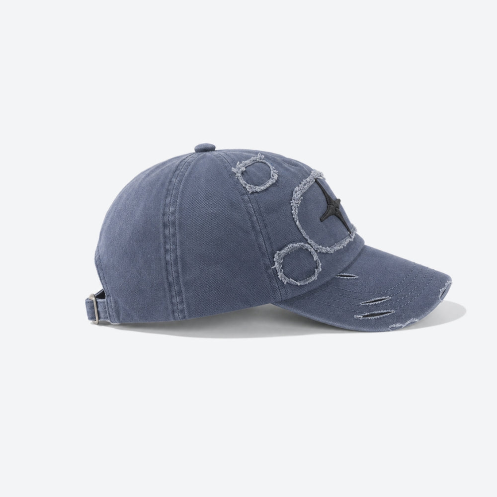 A washed blue denim baseball cap with distressed details, featuring a stylized embroidered face on the front and a curved brim, shown against a plain white background.