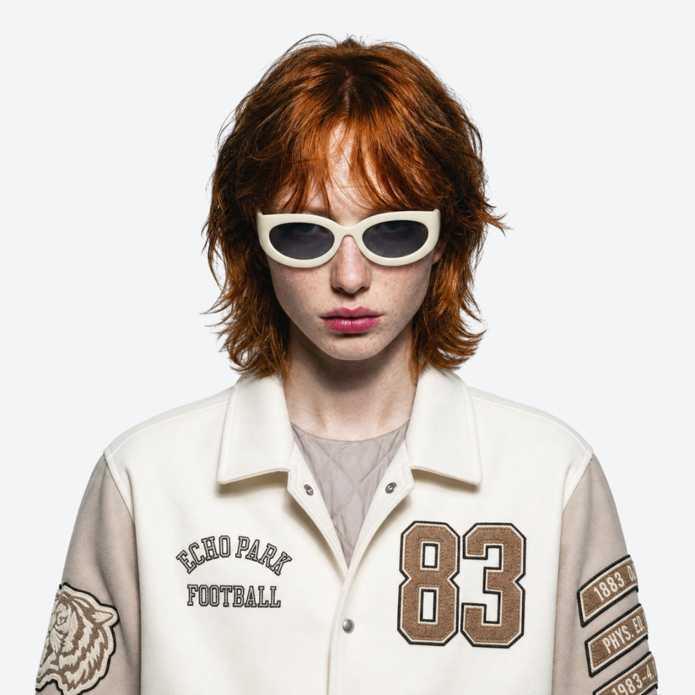 Person wearing a white jacket with VYSER Beige sunglasses with dark lenses, and red hair on a white background