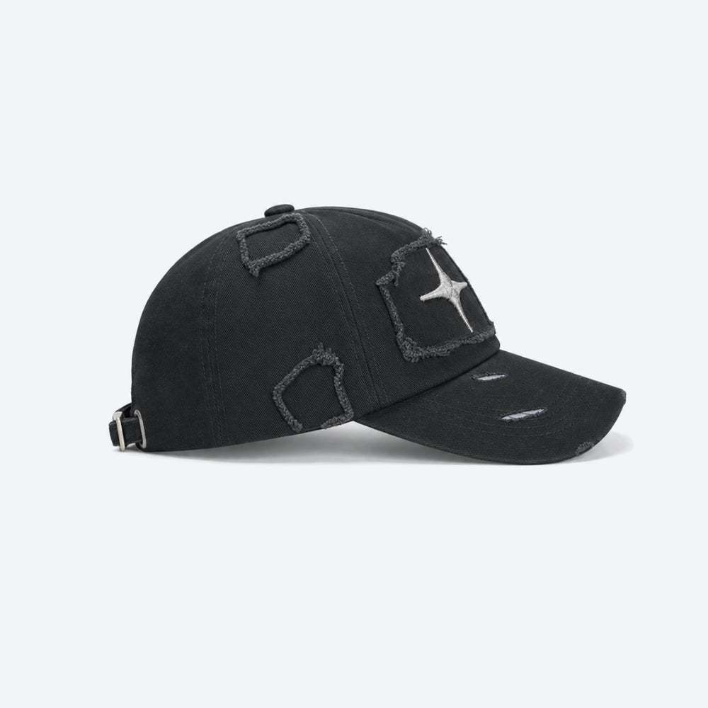 A black distressed baseball cap with unique frayed patch details on the front and brim, featuring a silver star emblem on the side, photographed on a light gray background.