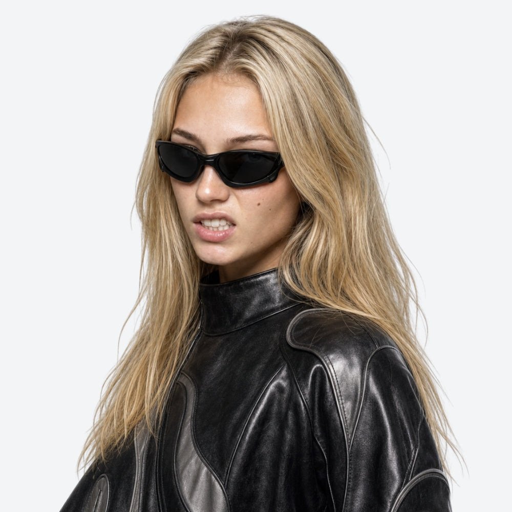 Woman wearing a black leather outfit and VYSER Sunglasses with a black frame and black lenses on a white background