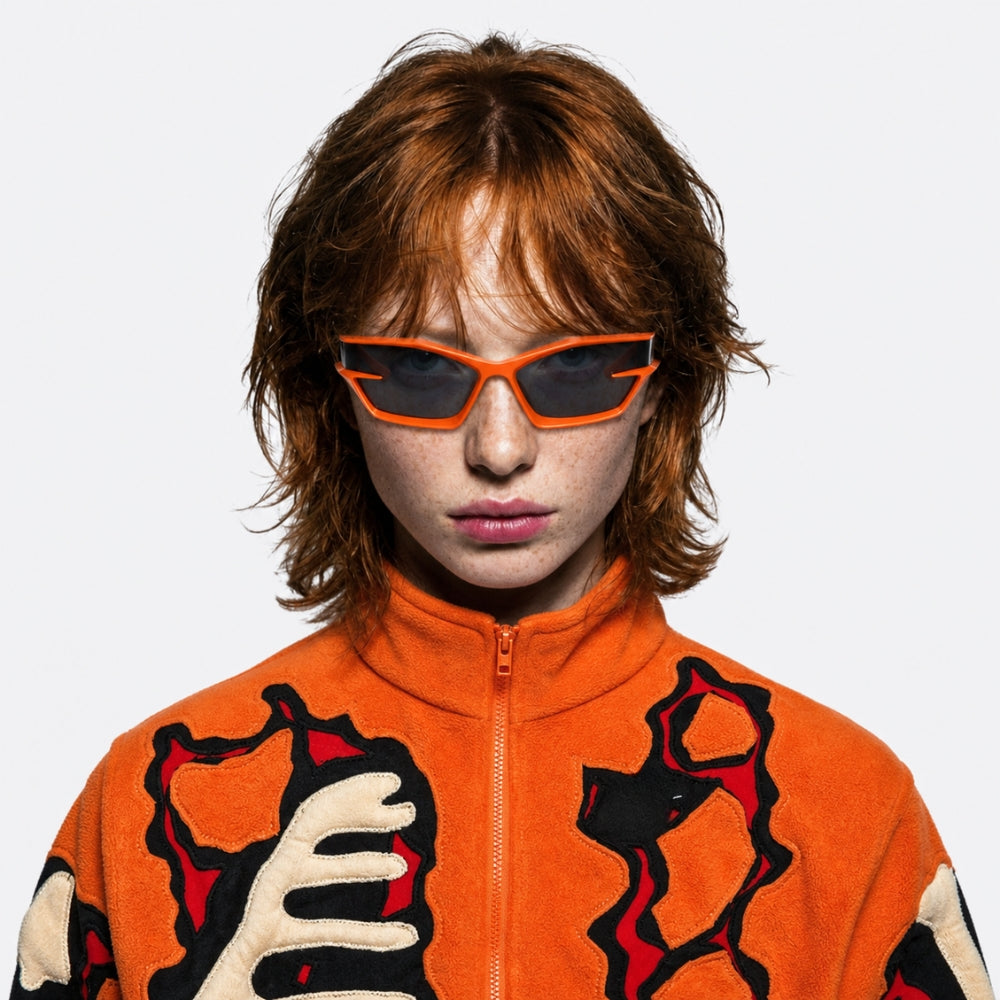 Person wearing an orange jacket with black and red patterns and VYSER Orange sunglasses with dark lenses on a white background