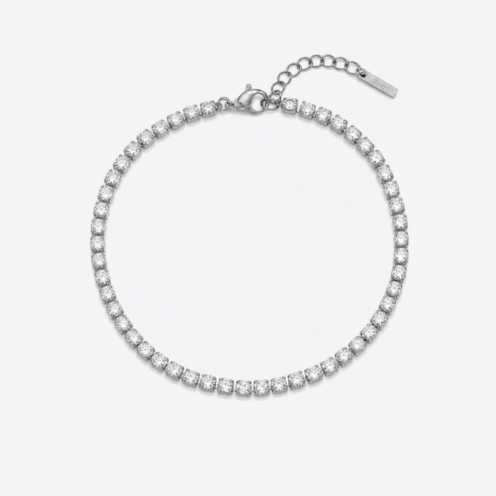 A silver tennis bracelet with a continuous row of clear round-cut stones, featuring a lobster clasp, extension chain, and a small brand tag, shown on a light gray background.