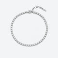 A silver tennis bracelet with a continuous row of clear round-cut stones, featuring a lobster clasp, extension chain, and a small brand tag, shown on a light gray background.