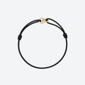 A minimalist black cord bracelet with a small gold interlocking rings clasp, displayed on a clean light gray background.