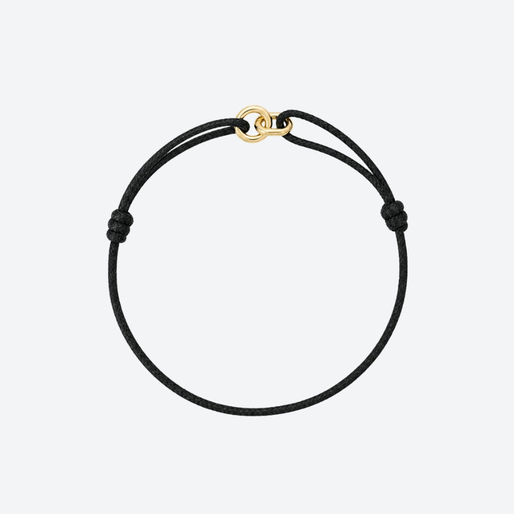 A minimalist black cord bracelet with a small gold interlocking rings clasp, displayed on a clean light gray background.