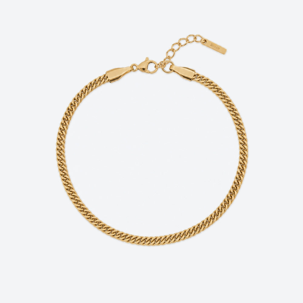 GOLD. A gold-toned Cuban curb chain bracelet with a lobster clasp, extender chain, and branded tag, light gray background.