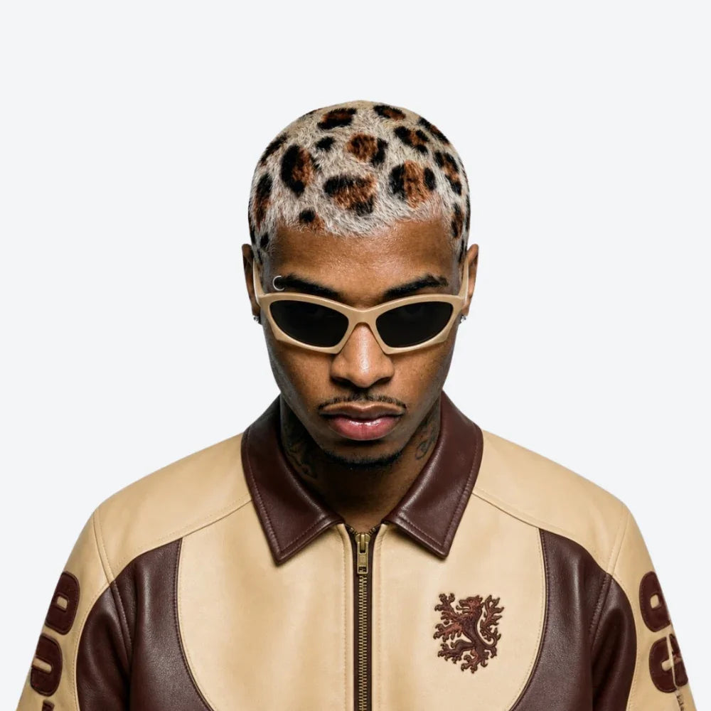 A man wearing a beige and brown leather jacket with a leopard-print pattern on his hair, styled with VYSER beige acetate sunglasses with sleek angular frame and dark gray lenses, minimalist streetwear style.