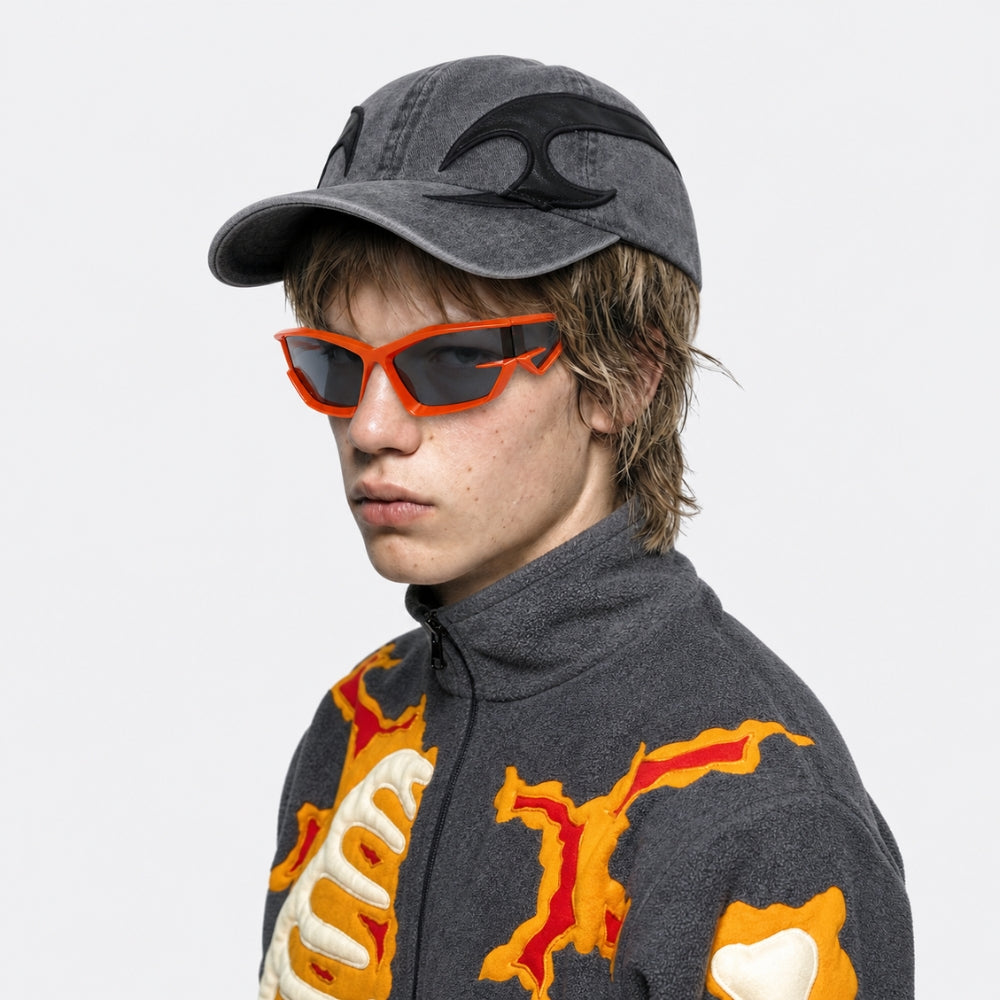 Person wearing a gray cap with a black logo and orange VYSER Orange sunglasses with dark lenses on a white background