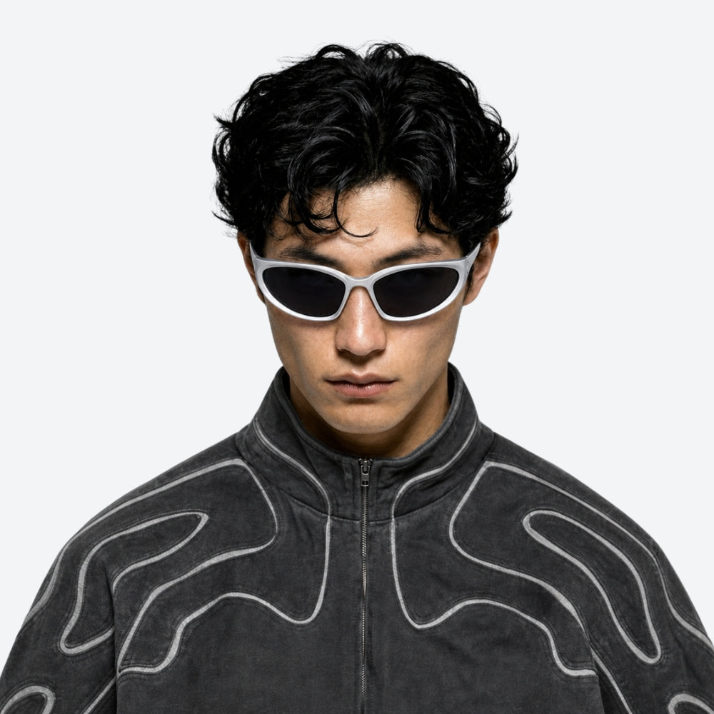 Person wearing a dark gray jacket with white patterns and VYSER silver sunglasses with black lenses on a white background