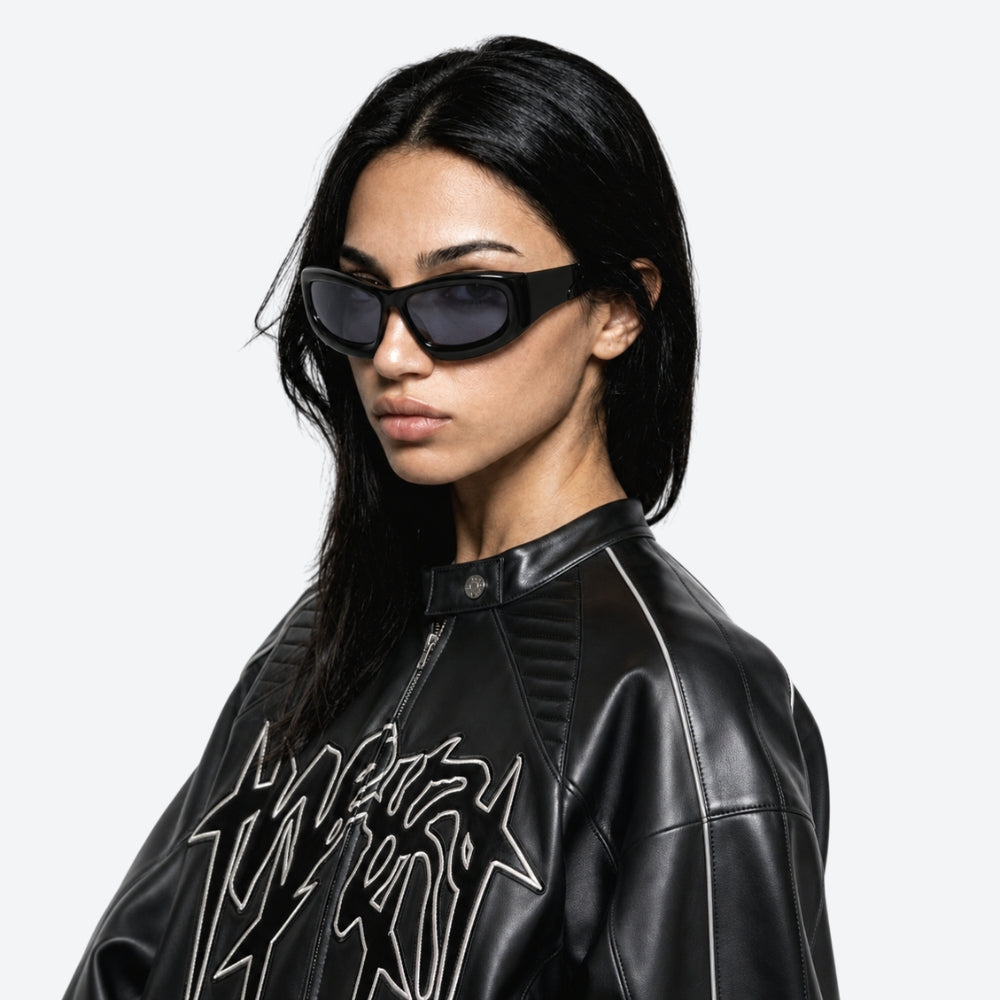 Person wearing a black leather jacket with a graphic design and VYSER Black sunglasses with dark lenses on a white background