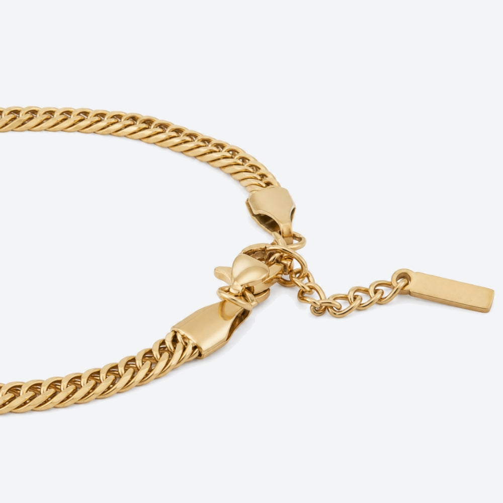 GOLD. A gold-toned Cuban chain bracelet with a lobster clasp, extender chain, and flat rectangular tag, light gray background.