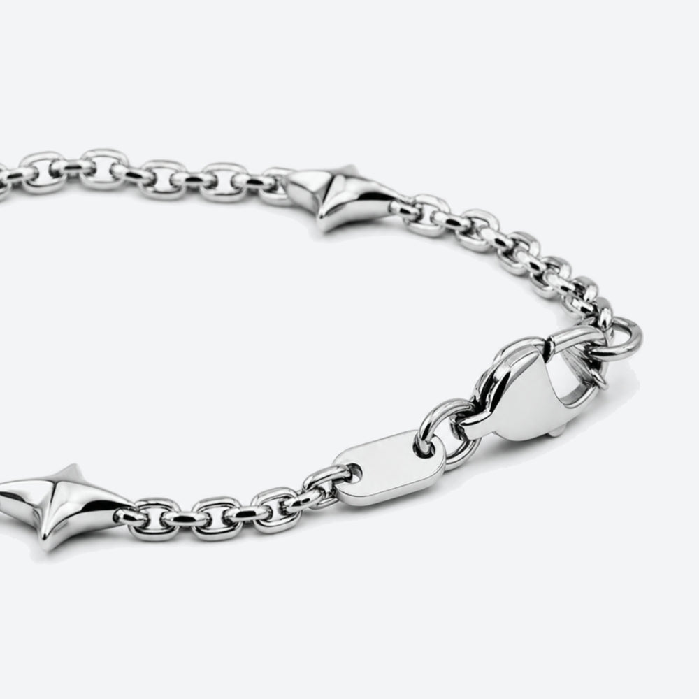 A close-up of a silver chain bracelet with pointed star-shaped links, a lobster clasp, and a small engraved tag showing the initials 'JV' on a light gray background.