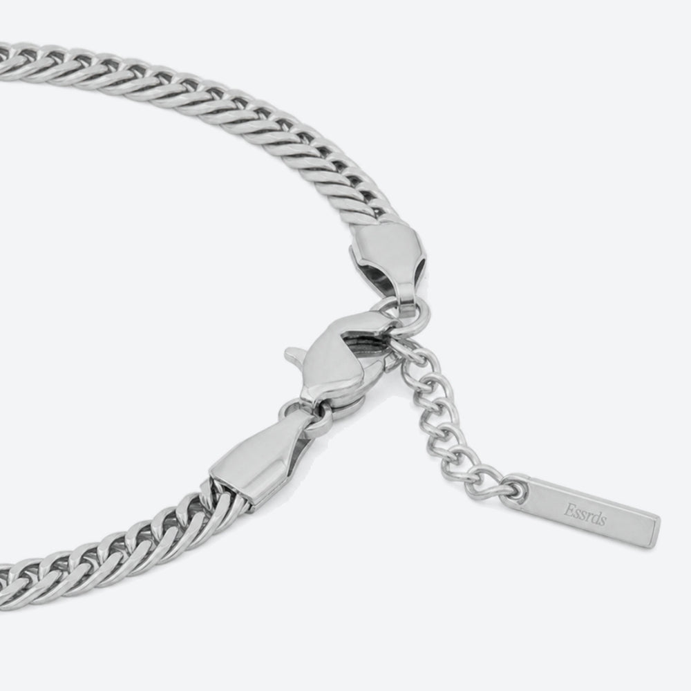 SILVER. A close-up of a silver Cuban chain bracelet with a lobster clasp, extender chain, and a brand tag, light gray background.