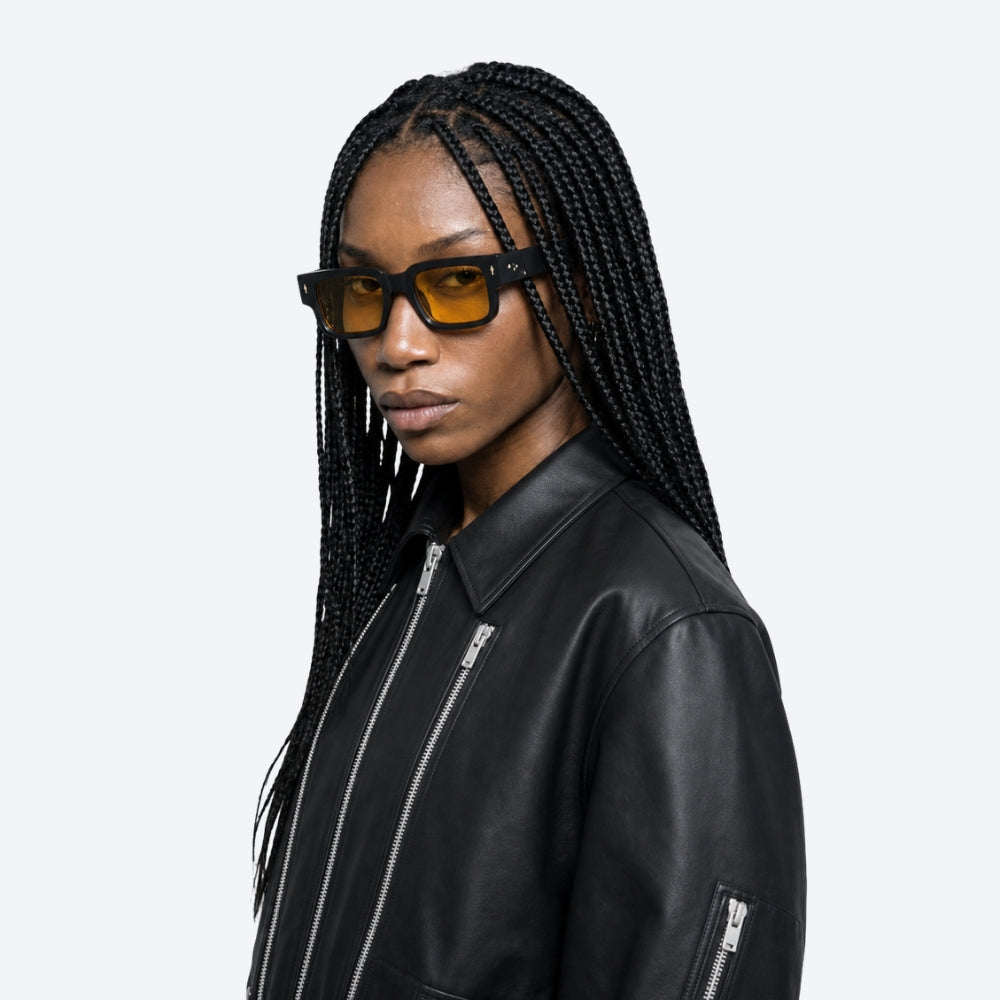 Person wearing a black leather jacket and VYSER Black sunglasses with orange lenses on a white background
