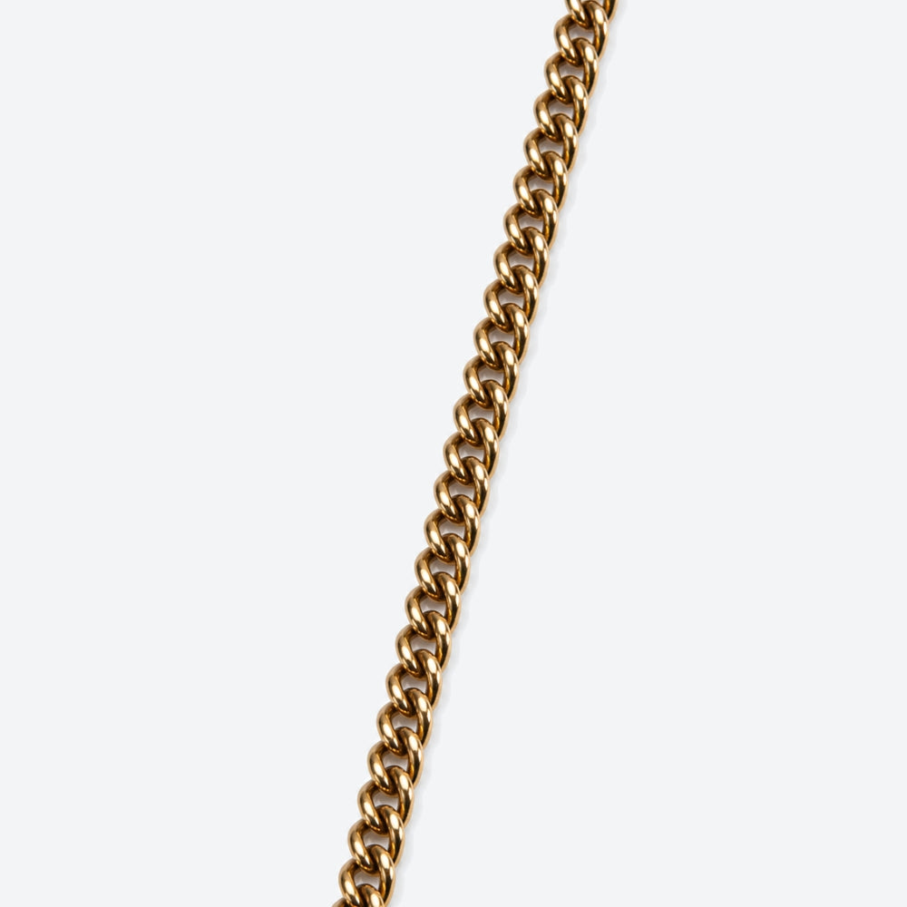 A close-up of a polished gold-tone curb chain running diagonally from the top right toward the bottom left on a light gray background.