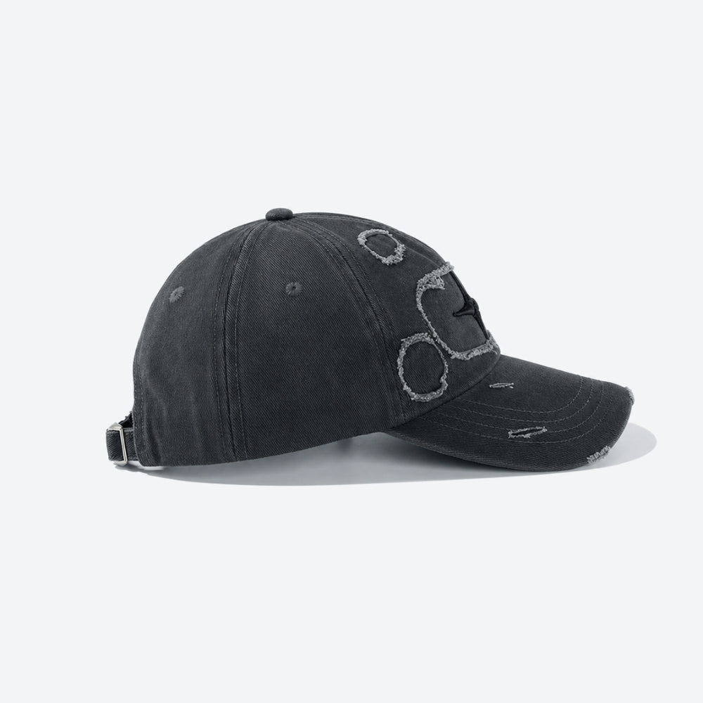 A washed black baseball cap with distressed details and a stylized embroidered graphic on the front, shown from a side profile on a light gray background.