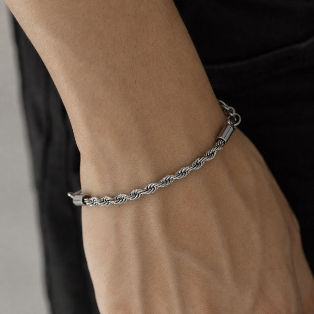 SILVER. A close-up of a person's wrist wearing a silver twisted rope chain bracelet, set against a black shirt background.