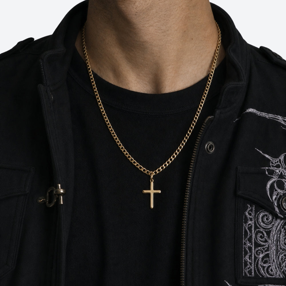 A close-up of a person wearing a gold chain necklace with a cross pendant, styled over a black t-shirt and a black jacket.