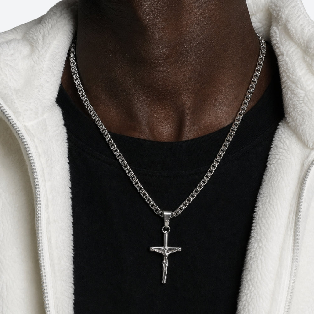 SILVER. A silver crucifix pendant necklace worn by a model in a black t-shirt and white fleece hoodie.