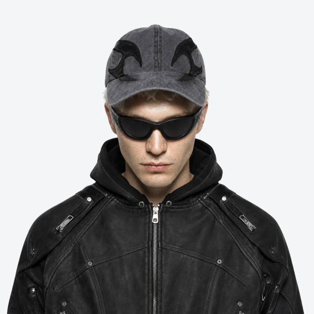 A model wearing a dark gray distressed baseball cap with black embroidered wing-like designs, VYSER Black wrap-around shield sunglasses with dark gray lenses, shown from a three-quarters angle on a light gray background.