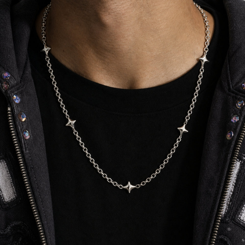 A silver chain necklace with five small star charms, worn by a person over a black t-shirt and a black jacket.