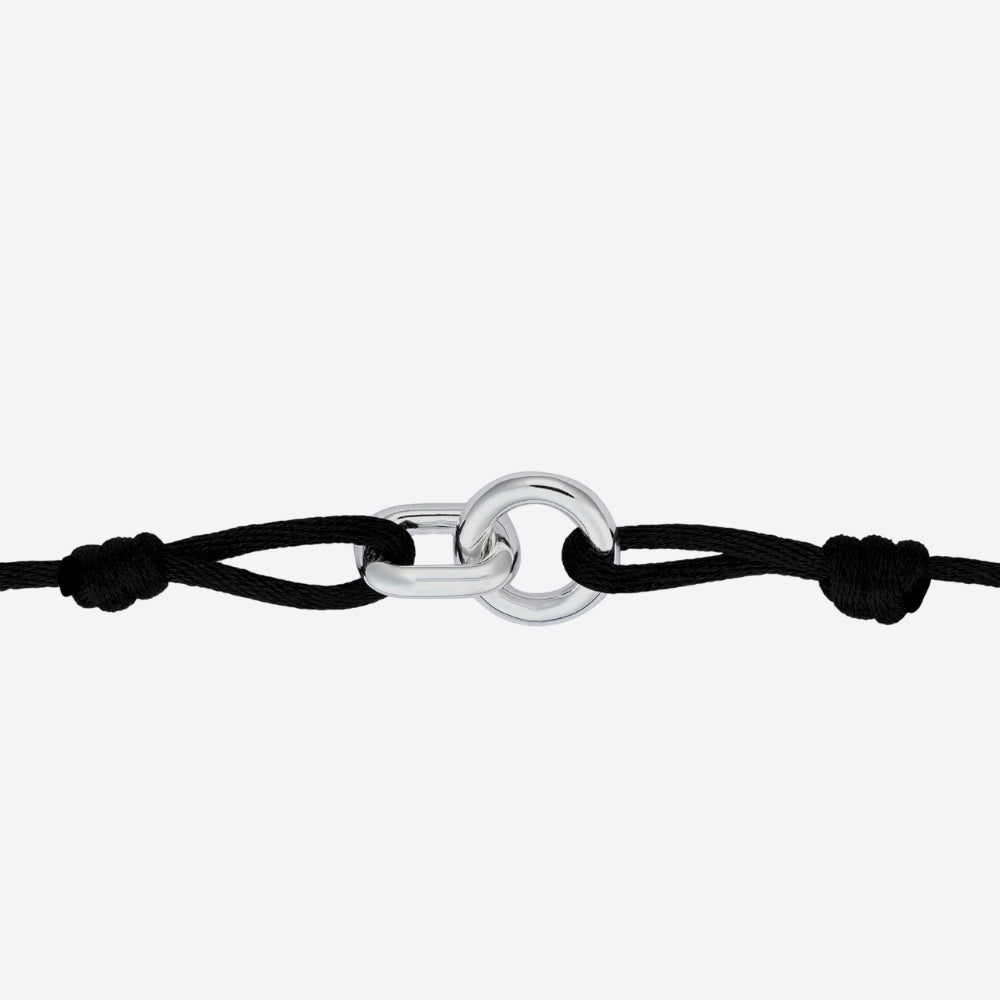 A minimalist black cord bracelet featuring a polished silver-toned metal link centerpiece, shown against a clean light gray background.
