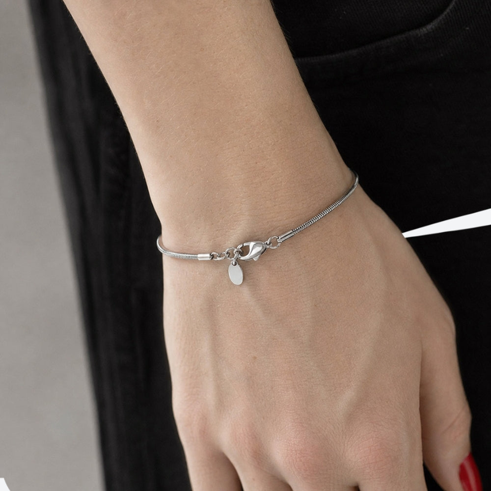 A delicate silver chain bracelet with a small oval charm, worn on a person's wrist against a black top background.