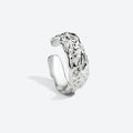 A polished silver open cuff ring with a highly textured, organic, wavy surface, photographed on a clean light gray background.