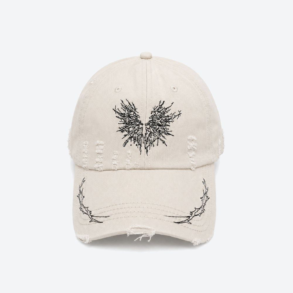A cream distressed baseball cap with a black embroidered moth on the front and thorn branch detailing along the brim, shown from the front