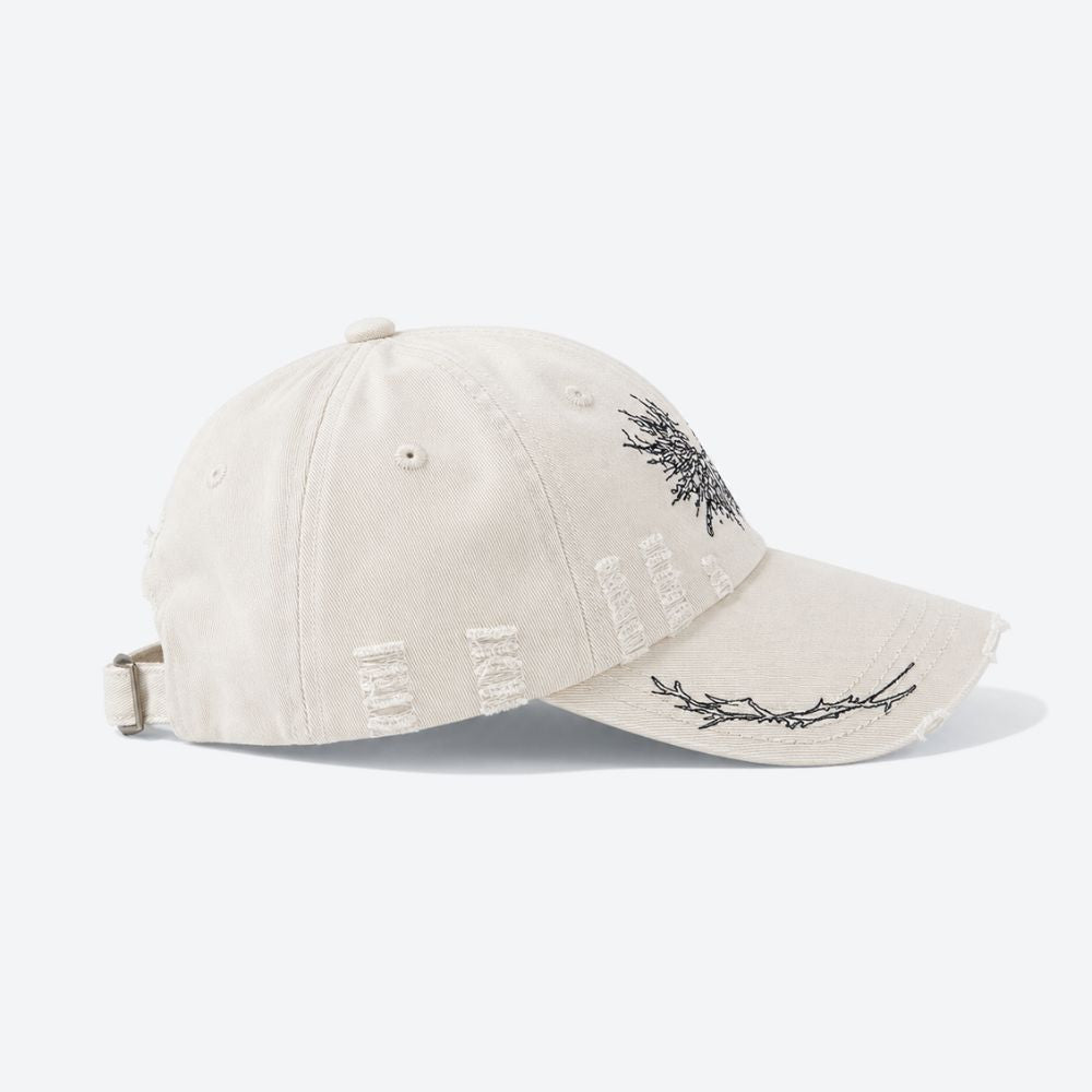 A cream distressed baseball cap with a black embroidered moth, shown from a three-quarter angle revealing the ripped detailing on the crown