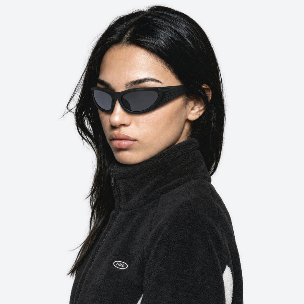 Person wearing VYSER Black wrap-around shield sunglasses with dark gray lenses, shown from a three-quarters angle on a light gray background.