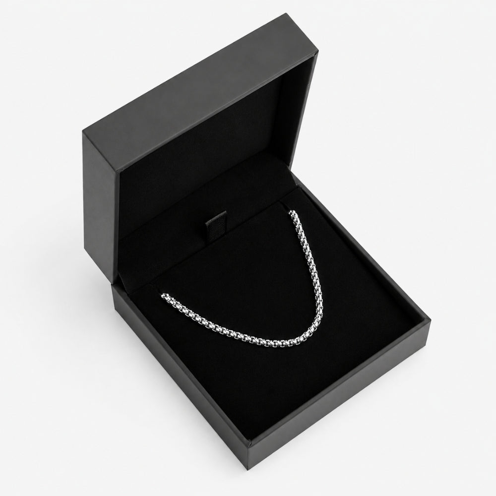 SILVER. A silver box chain necklace displayed inside an open black jewelry box, on a light gray background.