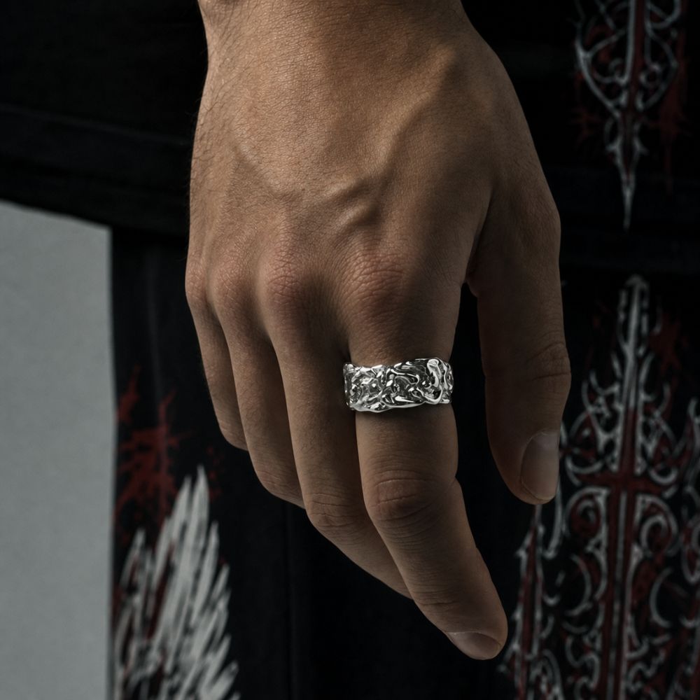 A close-up of a hand wearing a wide silver band ring with an intricate, textured gothic knot design, set against a dark background with a gothic pattern.