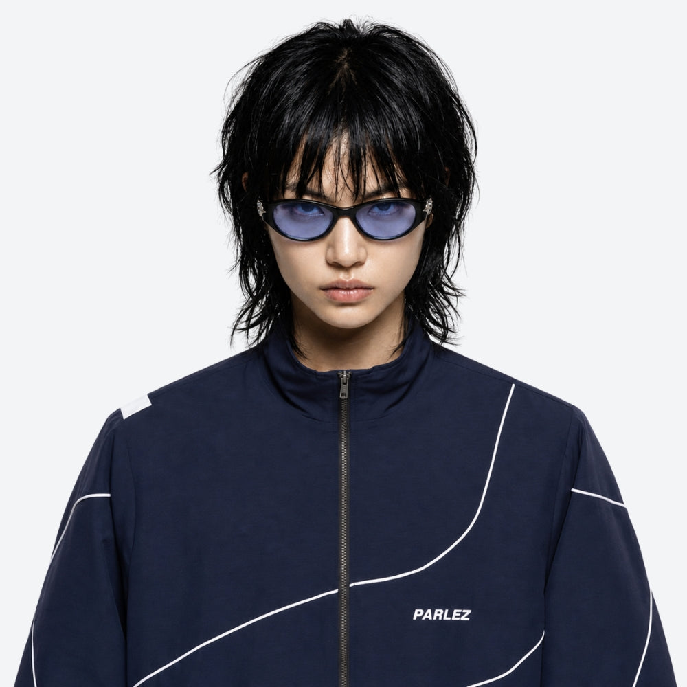 Person wearing a navy tracksuit with white accents and VYSER Black sunglasses with blue lenses on a white background
