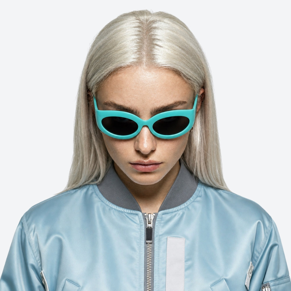 Person wearing VYSER Turquoise sunglasses with black lenses and a light blue jacket on a white background