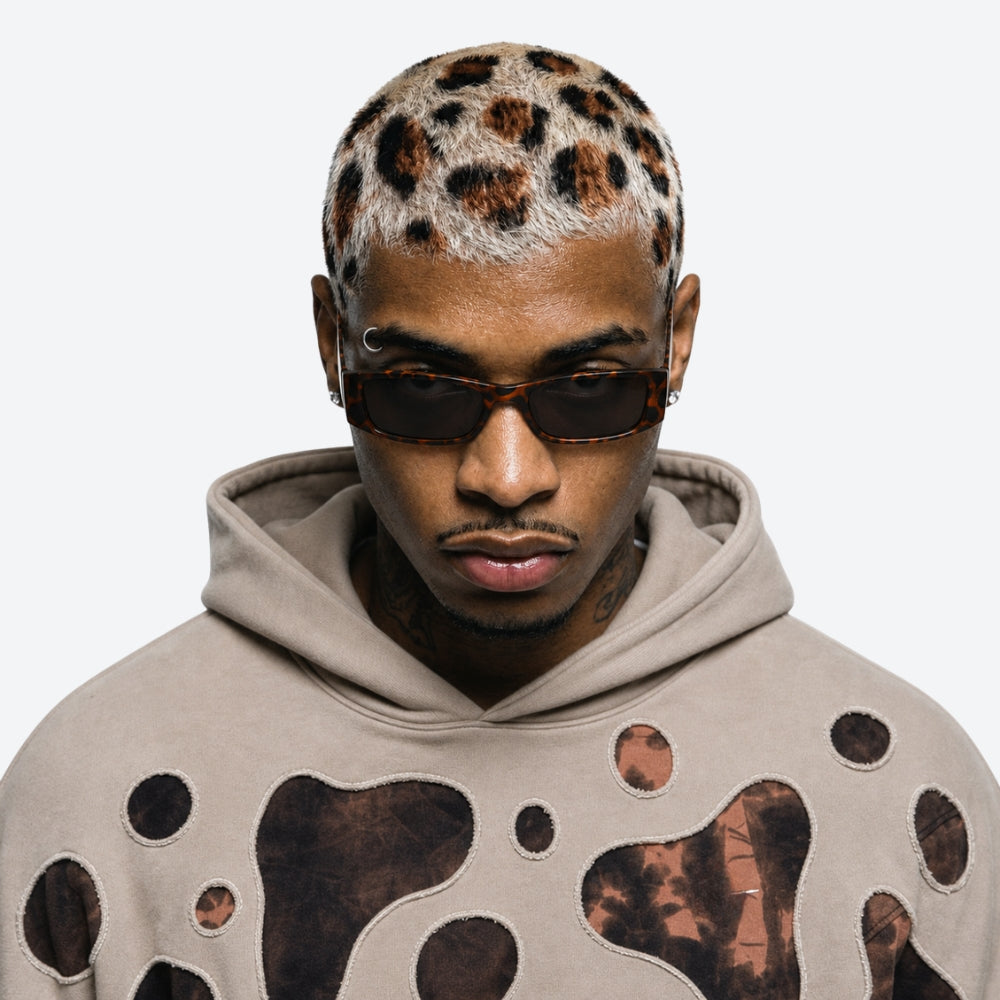 Man wearing a beige hoodie with brown abstract patterns and VYSER Sunglasses with leopard print frame on a white background