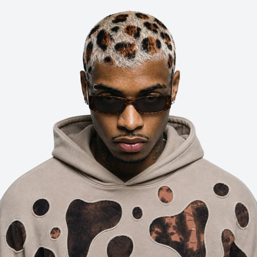 Man wearing a beige hoodie with brown abstract patterns and VYSER Sunglasses with leopard print frame on a white background