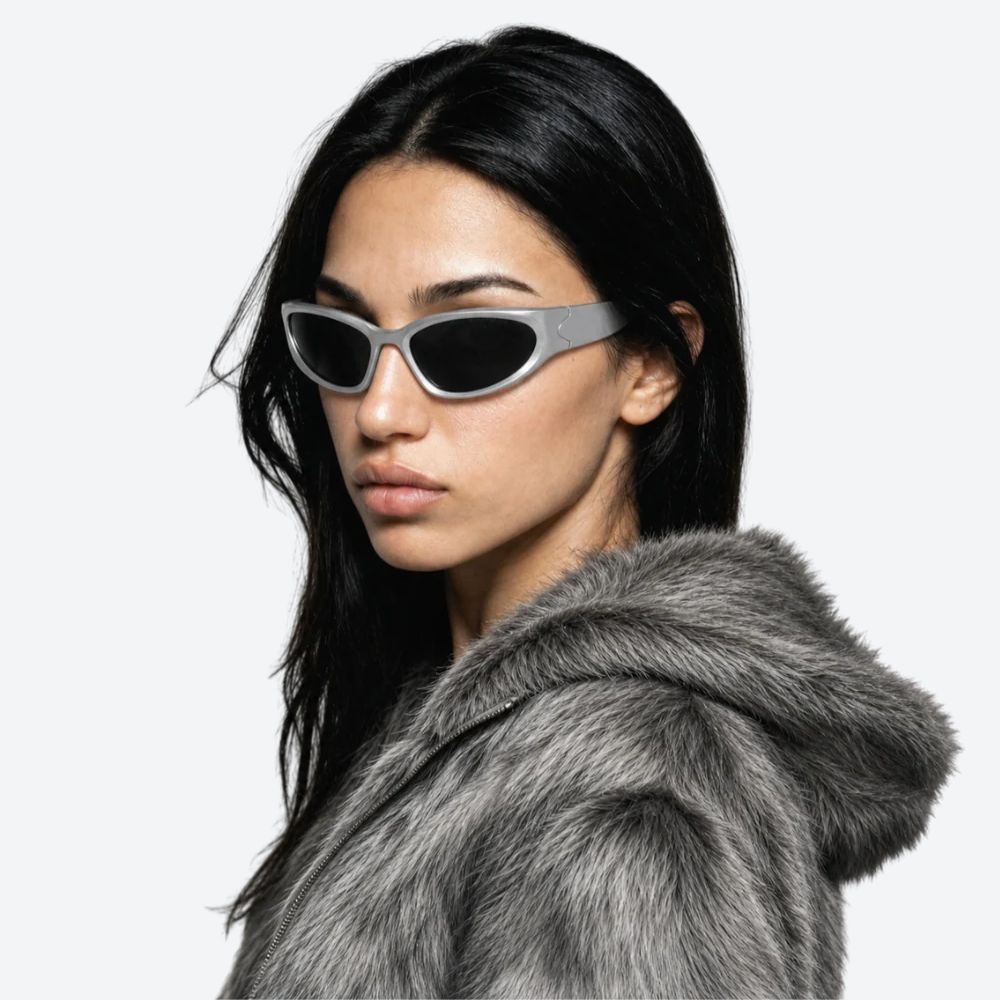 Woman wearing a fur coat and VYSER silver sunglasses with black lenses on a white background