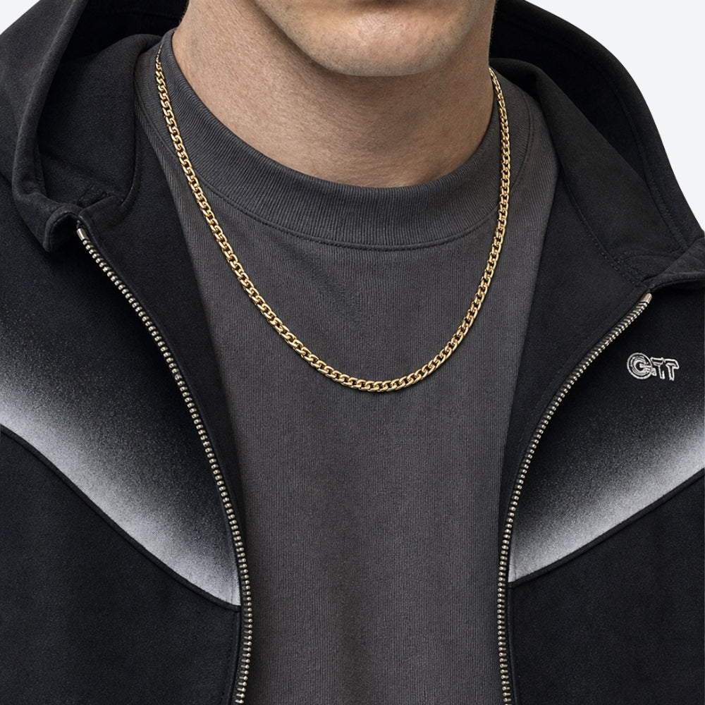 GOLD. A person wearing a gold box chain necklace over a dark gray t-shirt and black zip-up hoodie.