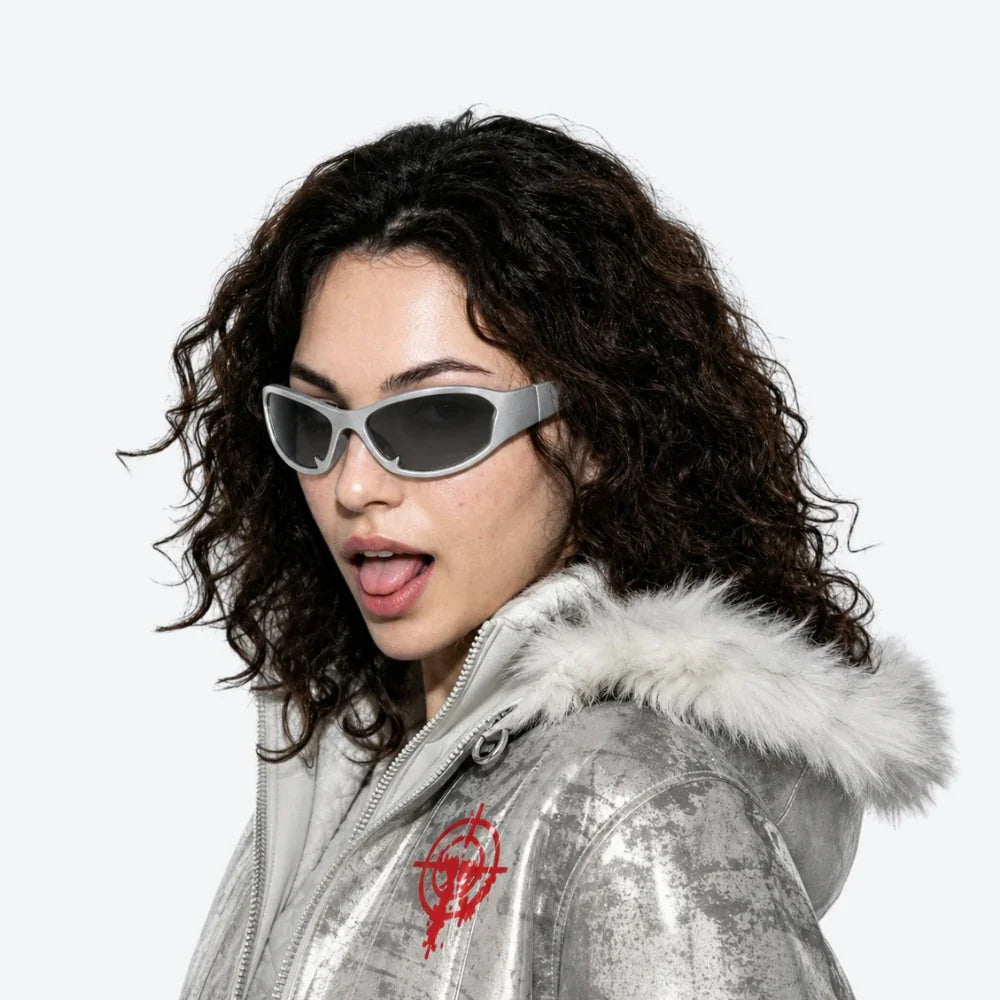 VYSER silver cat-eye sunglasses with dark lenses, styled with metallic jacket and faux fur hood.